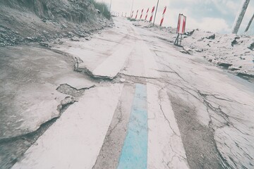 Cracked road with striped markings, leading uphill near construction