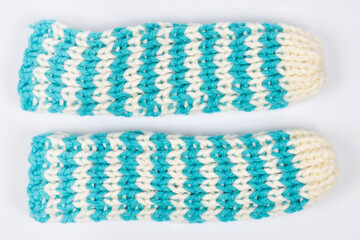 An overhead studio shot displays a pair of handmade, thick knitted warmers in a teal and cream two-color checkerboard pattern on a plain white background