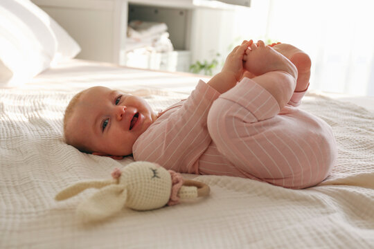 Adorable baby wearing pink pajamas lying on the back and playing with her feet. Copy space, background.
