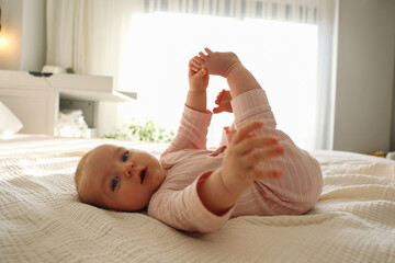 Adorable baby wearing pink pajamas lying on the back and playing with her feet. Copy space, background.