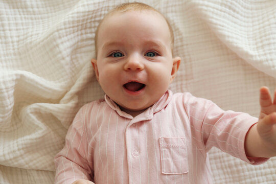 Top view shot of a joyful baby wearing pink pajamas lying on the back and laughing. Copy space, background.