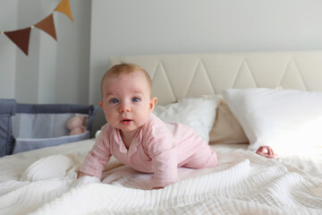 Playful baby learning to crawl on the bed. Copy space, background.