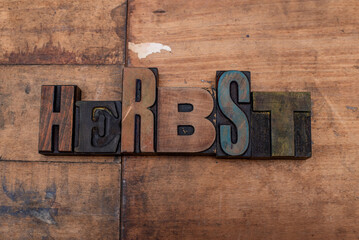 Fototapeta premium Das Wort Herbst / Autumn, mit alten Holzlettern, auf einem Untergrund aus Altholz ausgelegt. Teilweise mit alten Farbresten behaftet.
