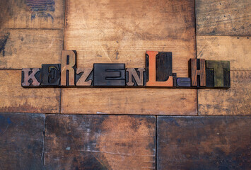 Das Wort Kerzenlicht, mit alten Lettern aus Holz ausgelegt, Der Untergrund besteht aus Altholz. Die Buchstaben sind alt, es gibt starke Gebrauchsspuren.