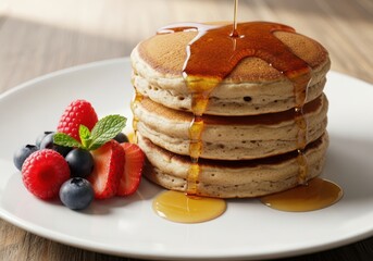 Stack of fluffy pancakes drizzled with golden syrup, served with fresh berries and mint on a white plate