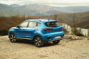 A photograph of the rear view with a partial left side angle of a blue SUV, set against the scenic backdrop of Lake Bovilla