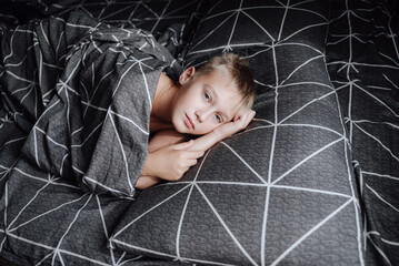 A handsome blond boy is lying in bed
