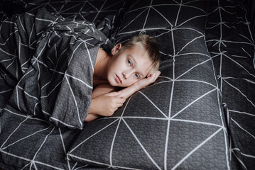 A handsome blond boy is lying in bed