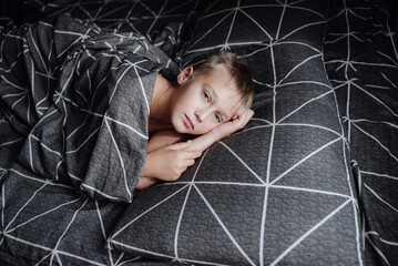 A handsome blond boy is lying in bed