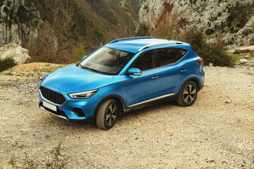 A photo capturing the front view with a slight left side angle of a blue SUV car, set against a natural background of mountains and greenery