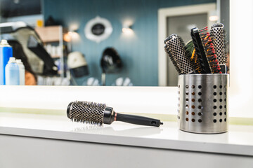 Hair salon brushes arranged on a clean counter with mirror reflections and warm lights highlighting a modern styling station