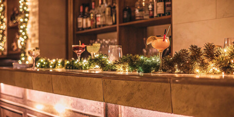 Two cocktails on bar counter with christmas garland and string lights for festive winter celebration suitable for seasonal greeting or holiday party composition