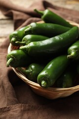 Ripe green jalapeno peppers in basket and towel on table, closeup