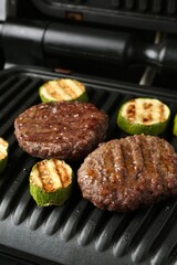 Electric grill with beef and zucchini on black table, closeup
