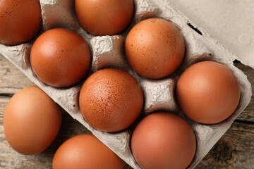 Raw chicken eggs in egg carton on wooden table, top view