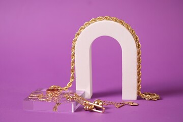 Stylish presentation of gold jewelry on violet background, closeup
