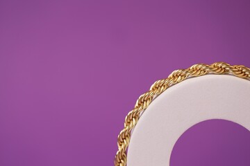 Stylish presentation of gold necklace on violet background, closeup. Space for text