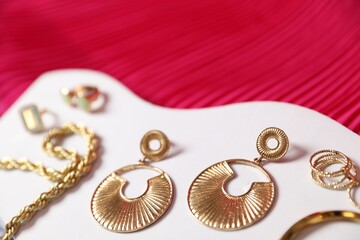 Stylish presentation of beautiful gold jewelry on pink fabric, closeup