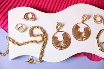Stylish presentation of beautiful gold jewelry on violet background, top view