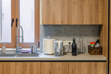 A modern kitchen interior with wooden cabinets, stone backsplash, and small appliances like a toaster and coffee maker