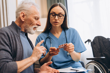 Nurse explaining medication to senior man during consultation sitting in living room at home