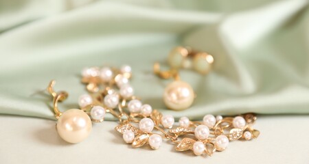 Beautiful gold jewelry and silk cloth on beige background, closeup