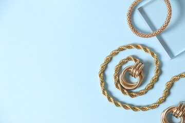 Beautiful gold jewelry on light blue background, flat lay. Space for text