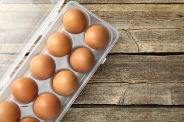 Raw chicken eggs in container on wooden table, top view. Space for text