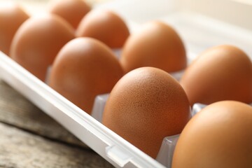 Raw chicken eggs in container on wooden table, closeup
