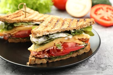 Tasty sandwiches with bacon, cheese, vegetables and sauce on grey textured table, closeup