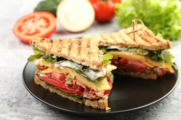 Tasty sandwiches with bacon, cheese, vegetables and sauce on grey textured table, closeup