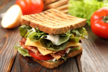 Tasty sandwich with bacon, cheese, vegetables and sauce on wooden table, closeup