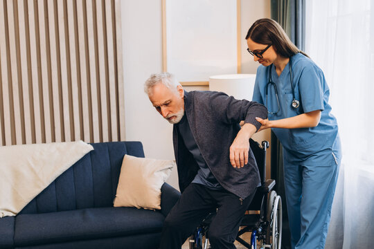Caregiver beautiful woman helping elderly man getting out wheelchair, training