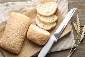 Fresh crispy ciabattas, knife and wheat ears on wooden table, flat lay