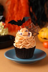 Delicious cupcake with chocolate web, bat topper and sprinkles on orange table against color background. Halloween celebration