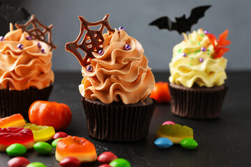 Delicious cupcake with chocolate web and colorful candies on dark textured table against grey background, closeup. Halloween celebration