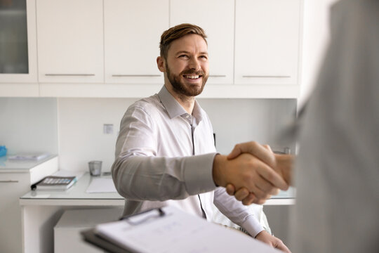 Smiling male patient handshake with therapist in clinic office