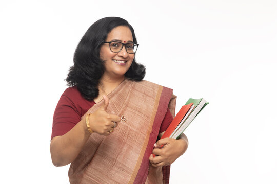 Portrait of Indian lady teacher showing thumbs up and wearing in saree  while holding notebooks. Confident traditional Indian woman against white background