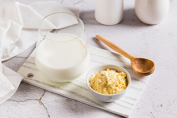 Bovine colostrum powder in a bowl and diluted drink in a glass on a table