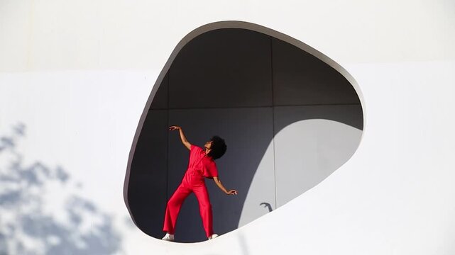 Afro woman in red dancing expressively in modern white building