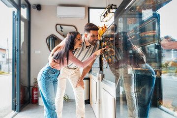 Happy young couple standing in bakery selecting fresh pastries.