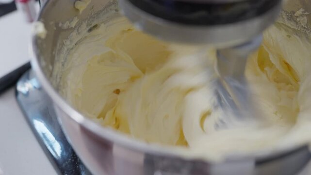 A Stand mixer whipping vanilla buttercream with the paddle attachment, as it turns and blends together making it creamy and smooth.