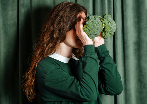 Woman holding broccoli as binoculars in front of green curtain