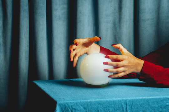 Hands of fortune teller with crystal ball on blue table indoors