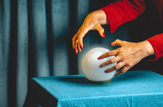Fortune teller hands above crystal ball on blue table indoors