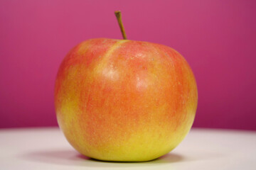 Ripe red yellow fresh apple on pink background, close-up