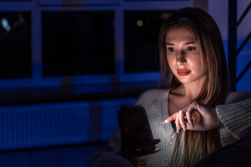 Young woman tapping smartphone screen by the window. Late touch.