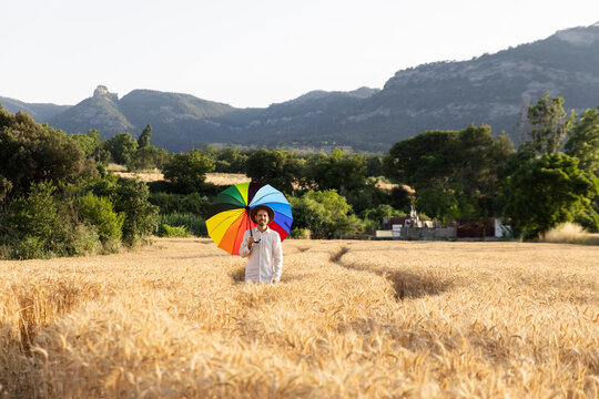 Man with rainbow umbrella standing in wheat field at sunset
