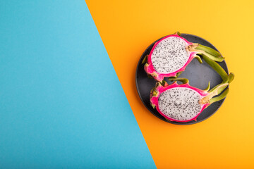 Ripe Pitaya on blue plate on blue and orange pastel paper, top view, copy space