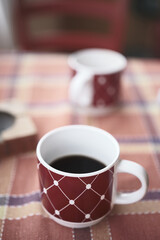 Morning coffee in patterned red mug on soft pastel tablecloth, cozy lifestyle and hygge concept